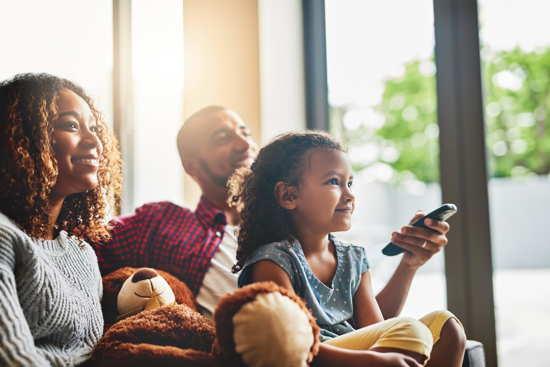 Happy young family of three watching tv from the sofa at home